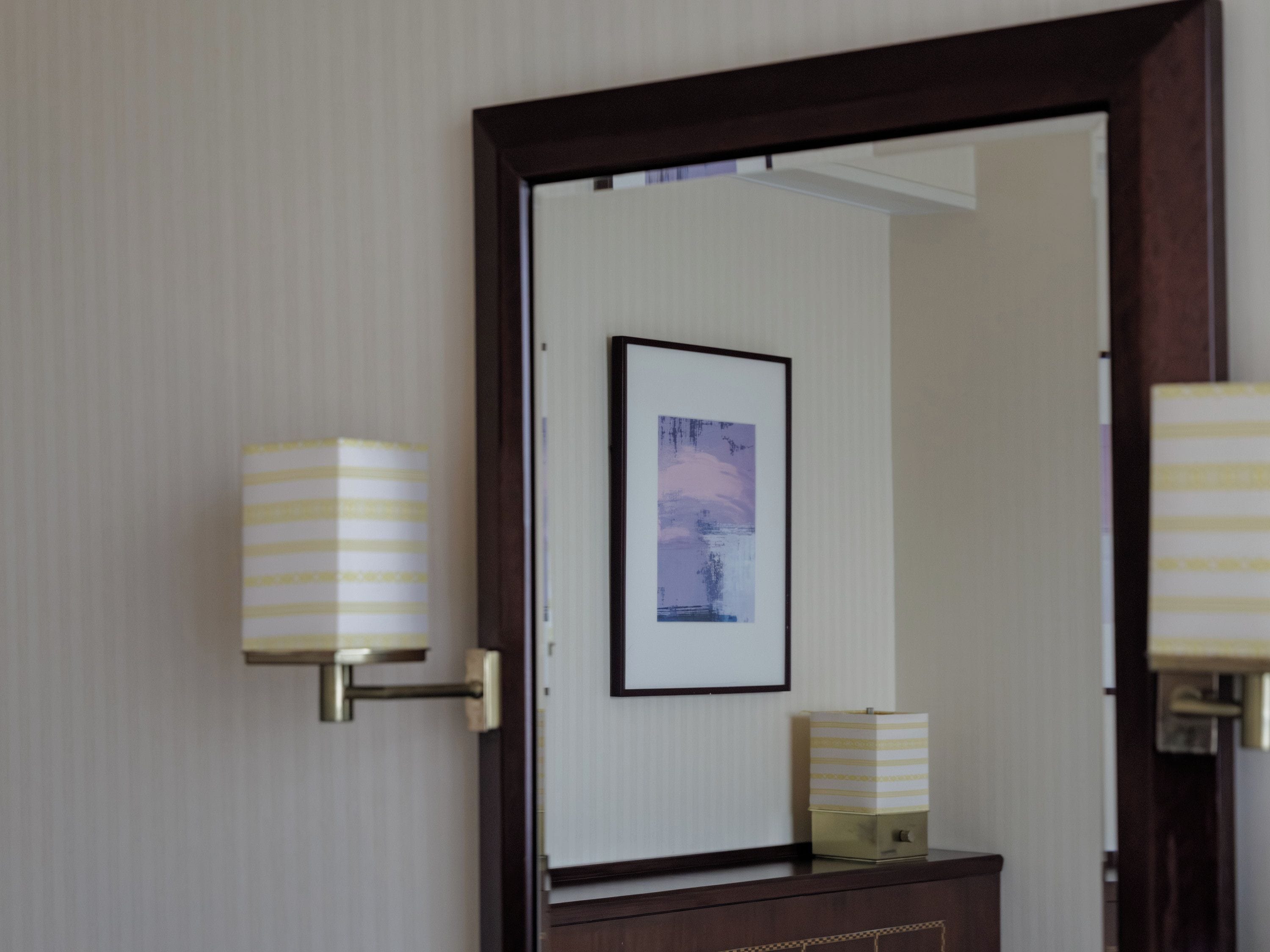 A room with a door, a framed picture on the wall, and two wall-mounted lamps.