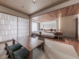 A hotel room with a large bed, a desk, and a dining area with chairs and a table.