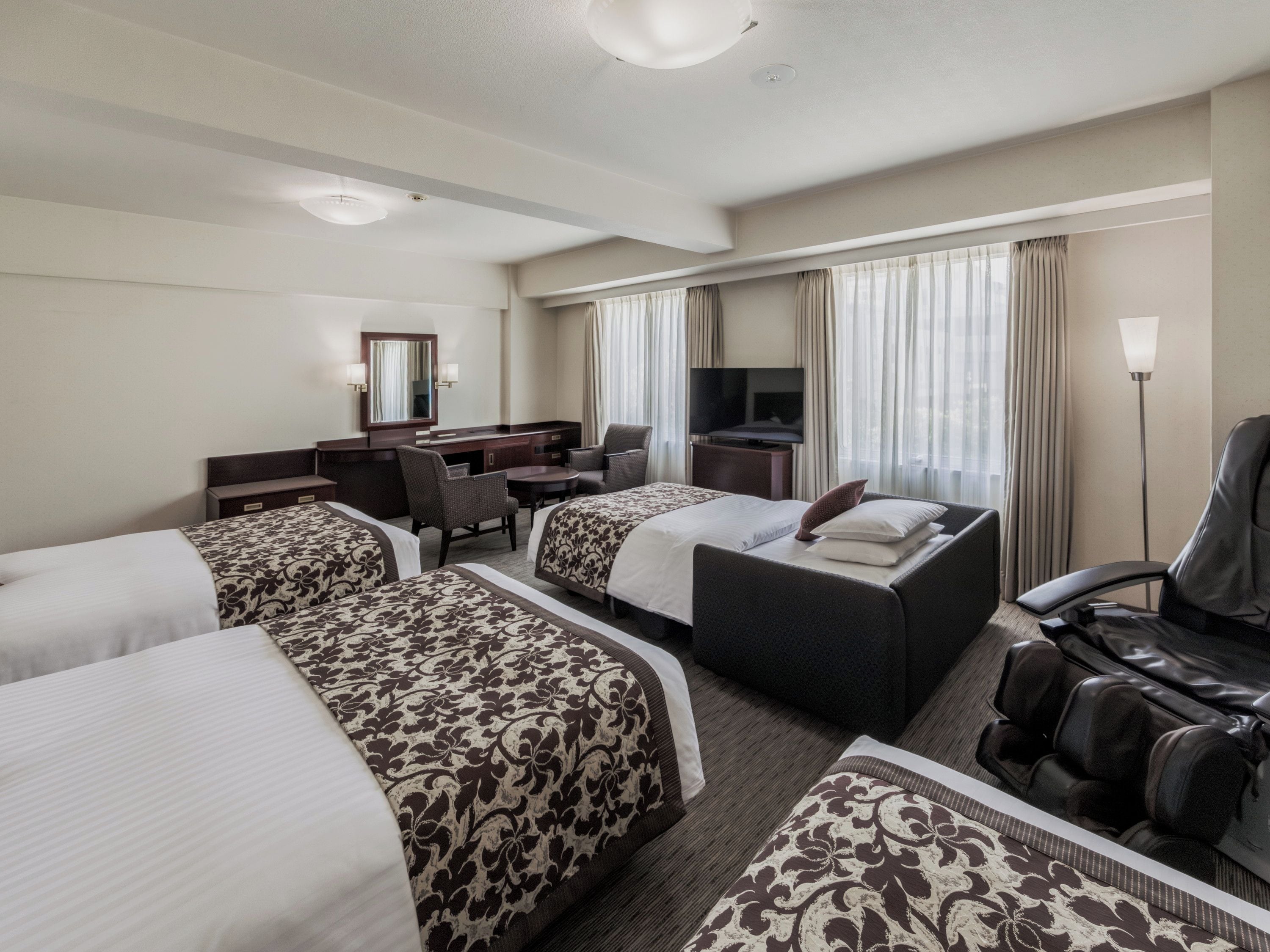 A hotel room with two beds, a desk, a chair, a sofa, and a TV.
