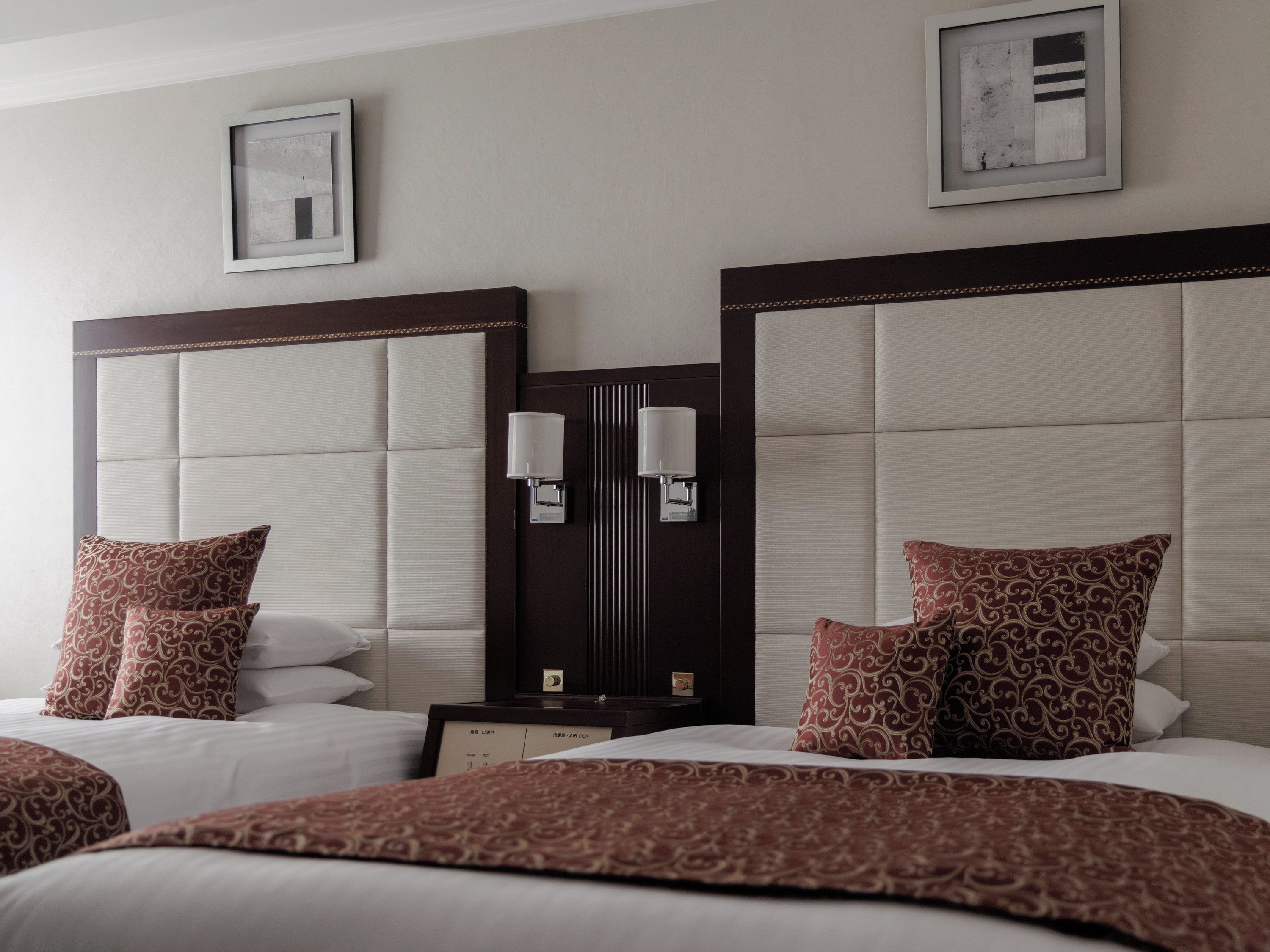 A hotel room with two beds, a nightstand, wall-mounted lamps, and framed artwork.