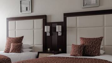 A hotel room with two beds, a nightstand, wall-mounted lamps, and framed artwork.