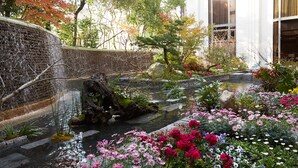 A serene garden with a stone wall, a small pond, and a variety of flowers. - Nishitetsu Grand Hotel (Fukuoka)