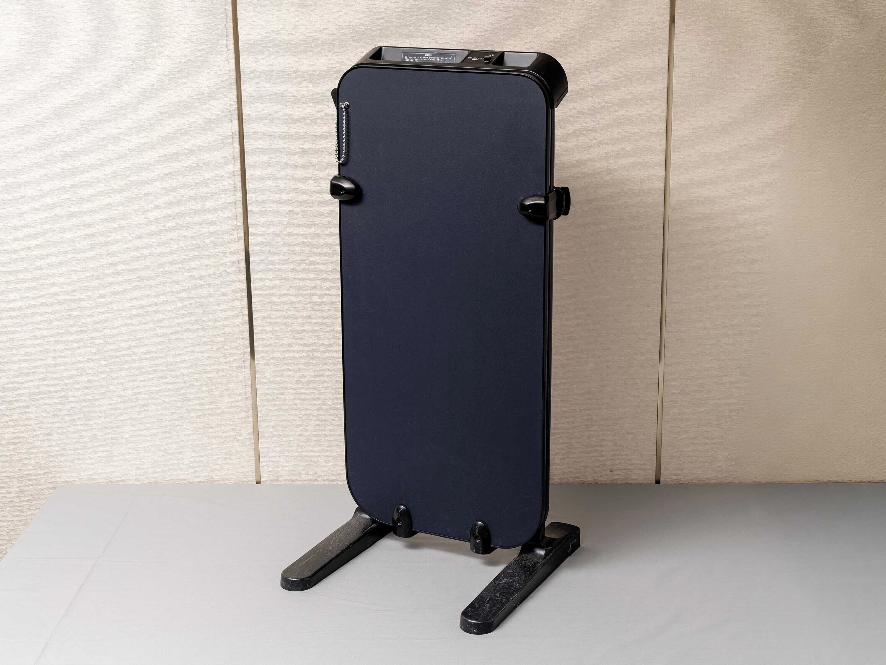 A dark-colored suitcase with a handle and wheels, standing upright on a flat surface.