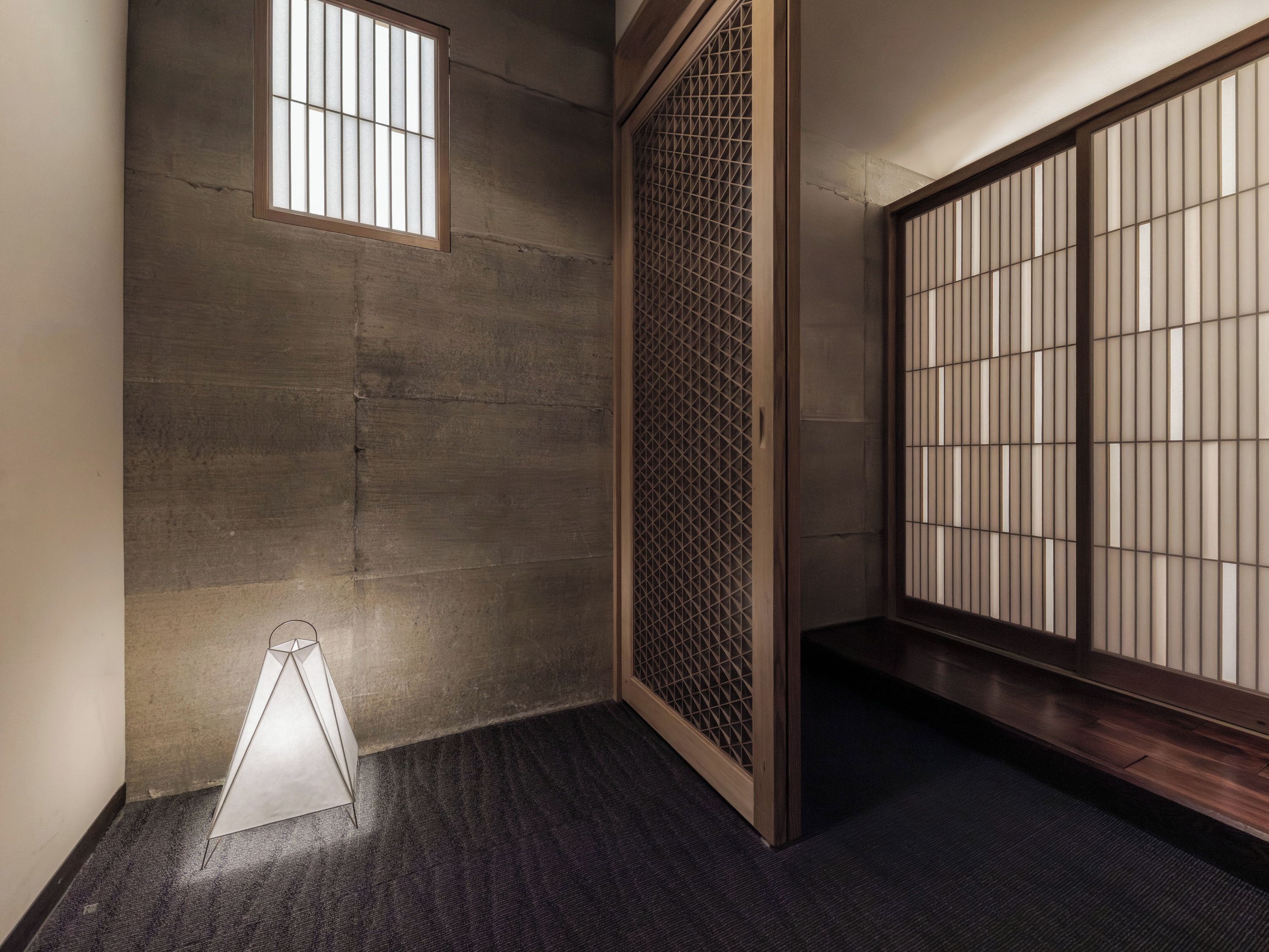 A room with a dark carpet, a wooden floor, a sliding door with a grid pattern, and a small window.