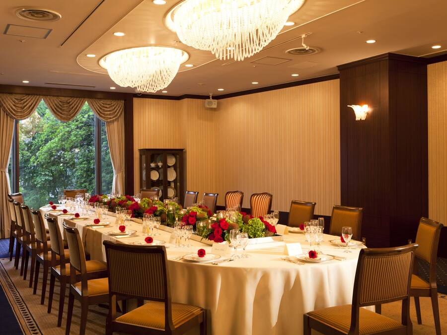 A banquet hall with a long table set for a formal event, surrounded by chairs.