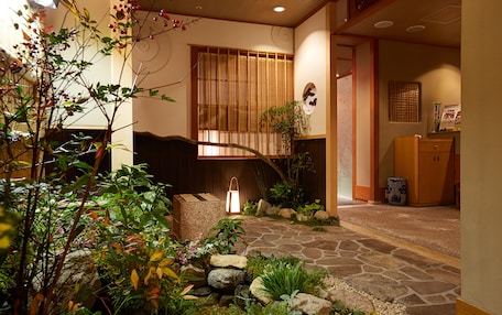 A traditional Japanese-style interior with a stone pathway leading to a wooden door, surrounded by lush greenery and a lantern.