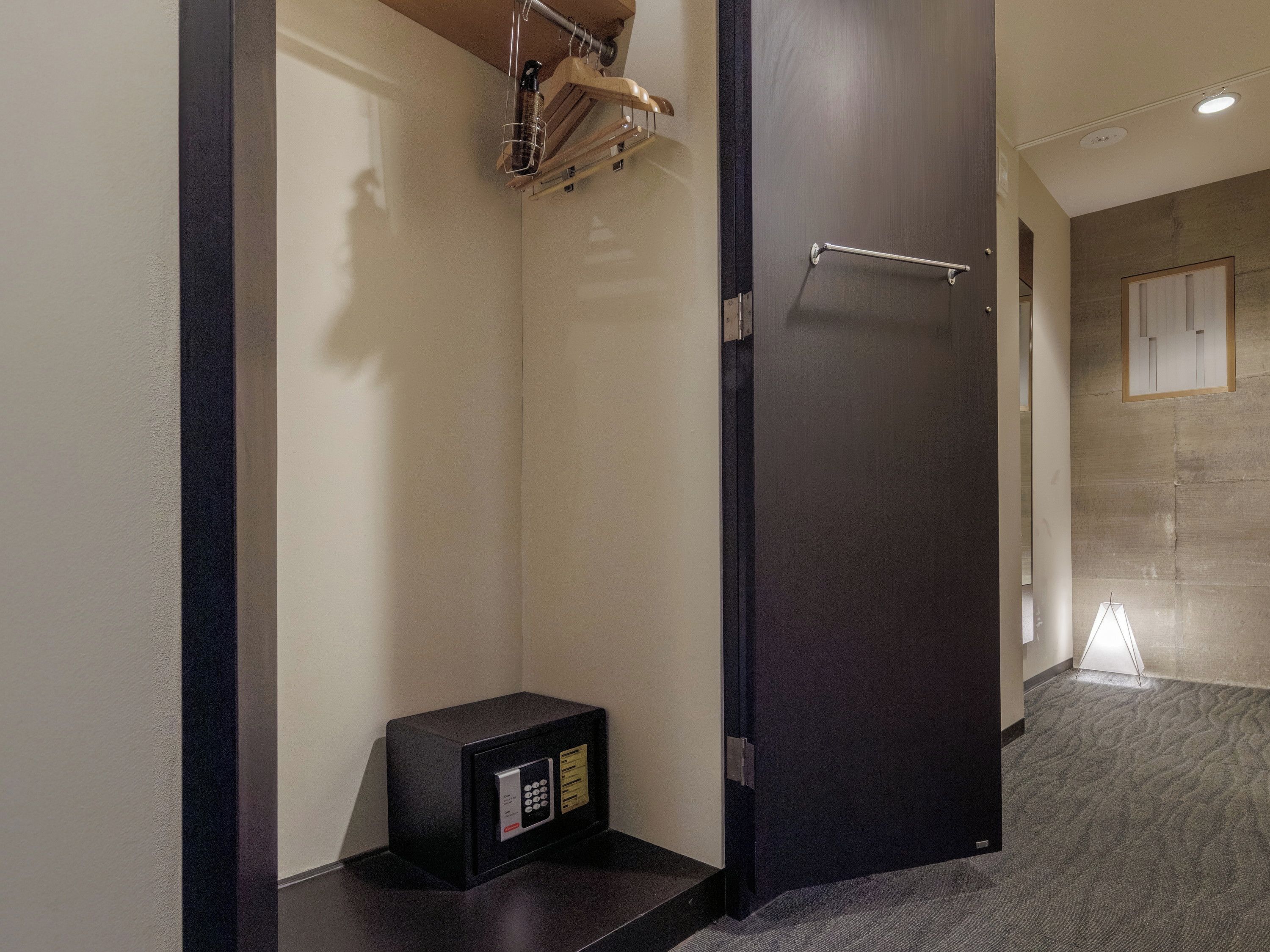 Habitación de hotel con una caja fuerte negra, un perchero y una puerta que da a otra habitación.