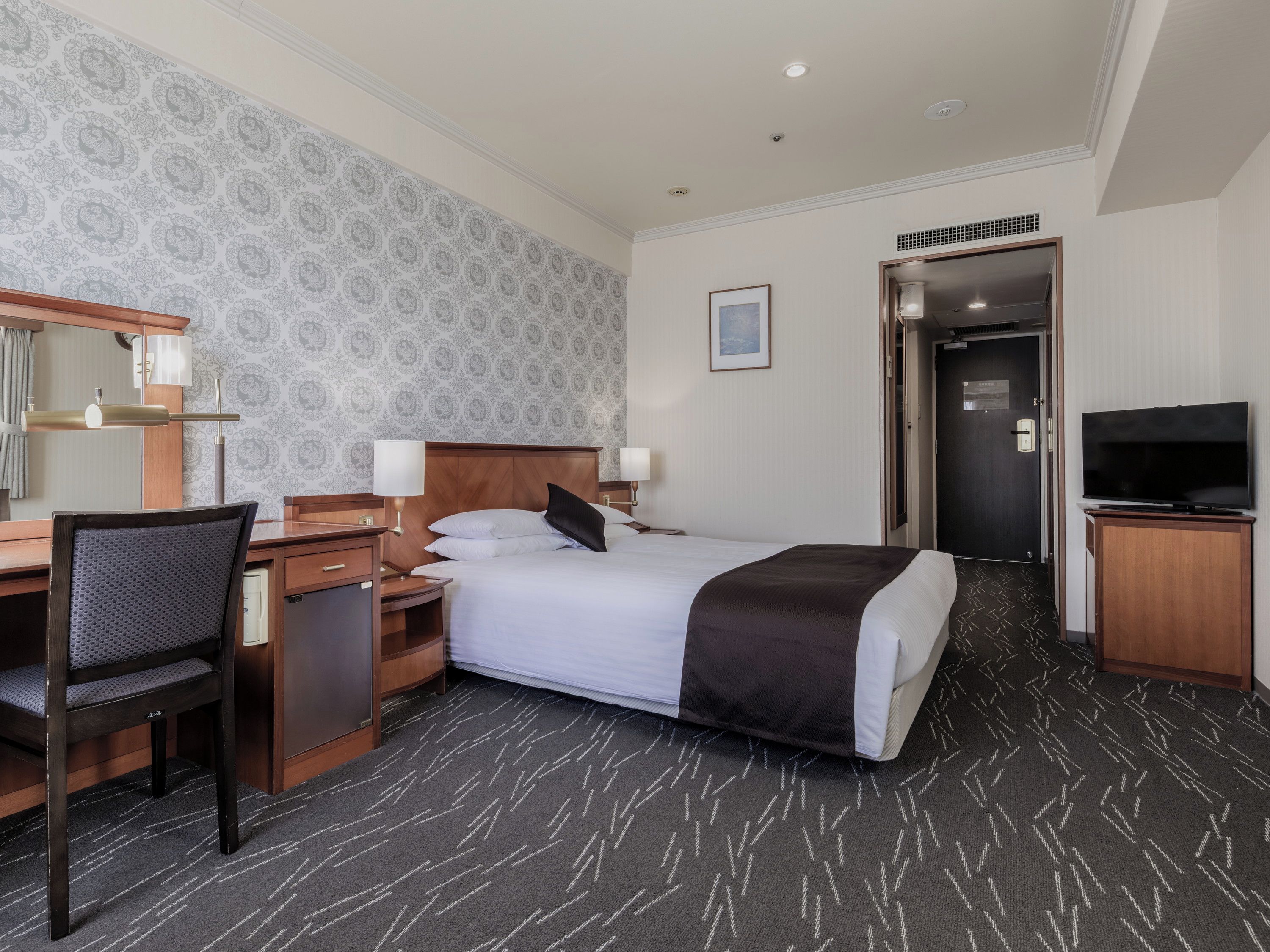 A hotel room with a bed, desk, chair, television, and a door leading to another room.