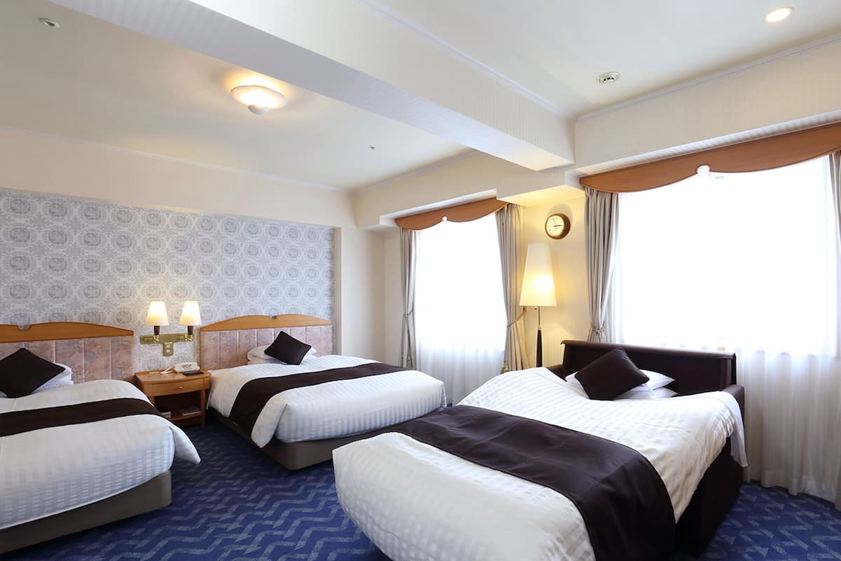 A hotel room with three beds, a clock, a lamp, and a patterned wall.