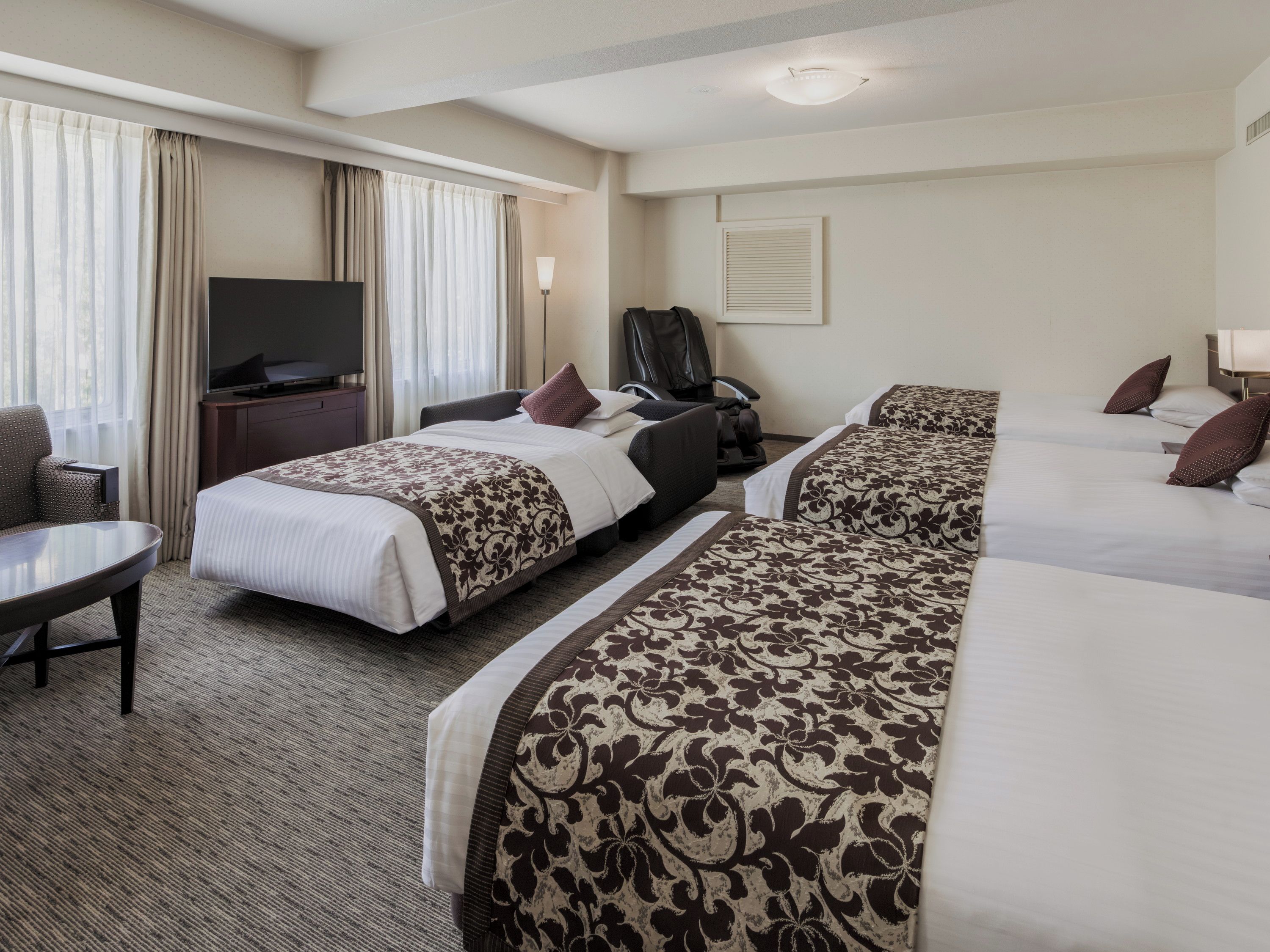 A hotel room with a bed, a desk, a chair, a television, and a window with curtains.