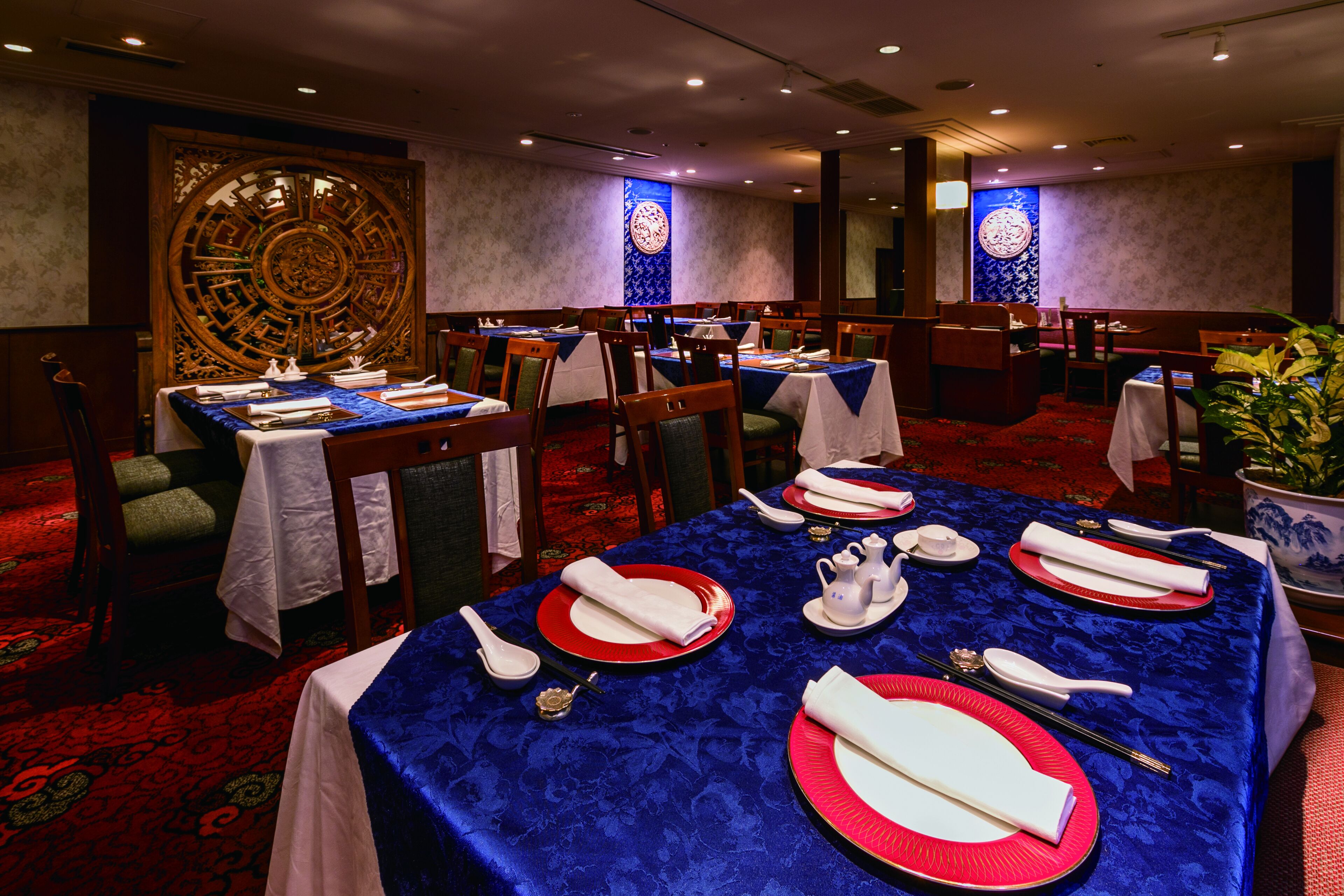 Un restaurante con mesas dispuestas para comer, con manteles azules y platos rojos.