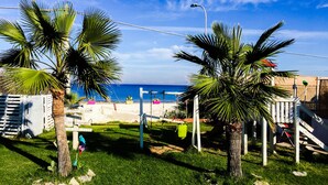 A grassy area with palm trees and a view of the sea. - Case Playa (Balestrate)