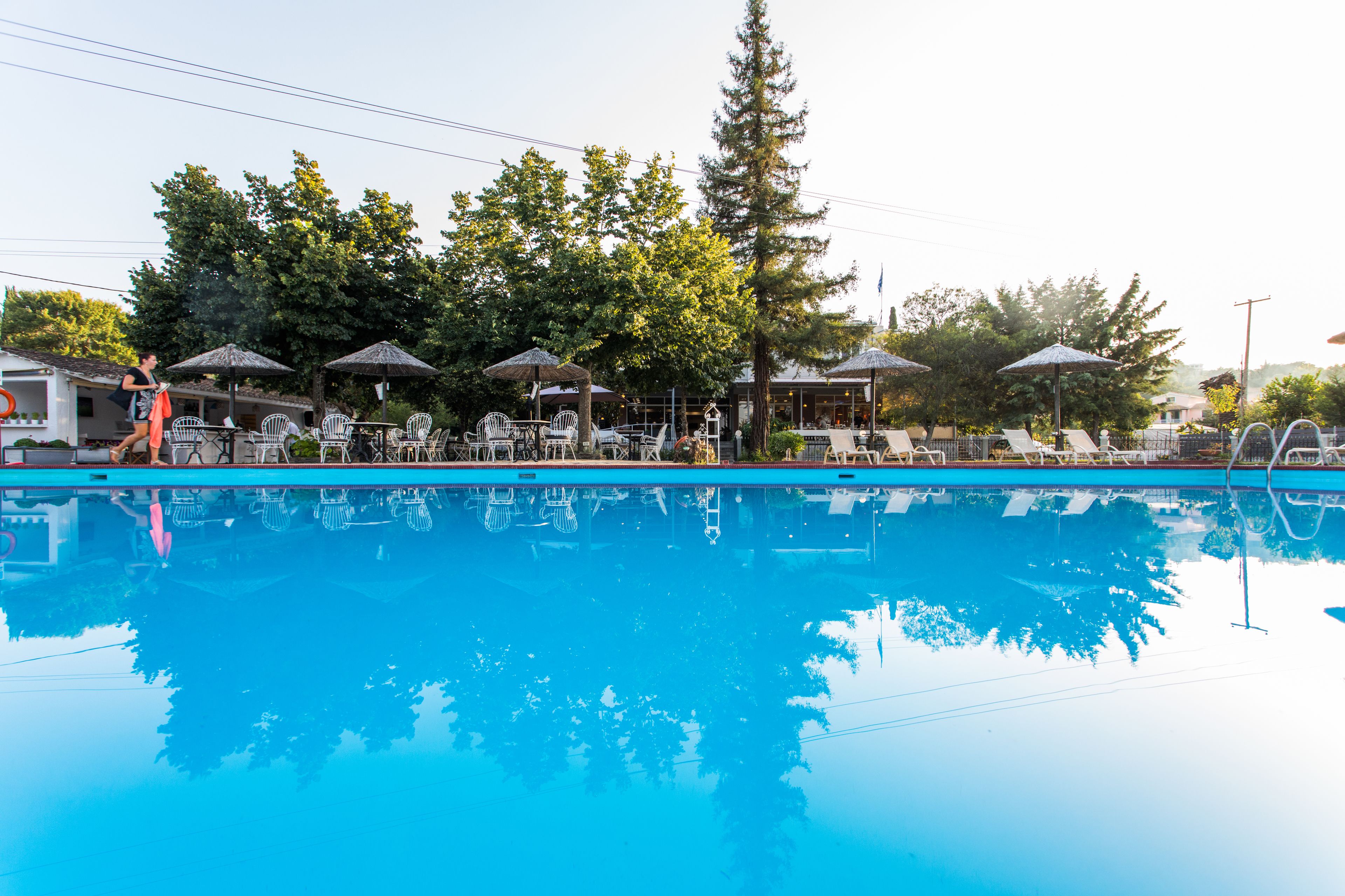 Une piscine entourée d’arbres, avec des chaises longues et des parasols, et un bâtiment visible au loin.