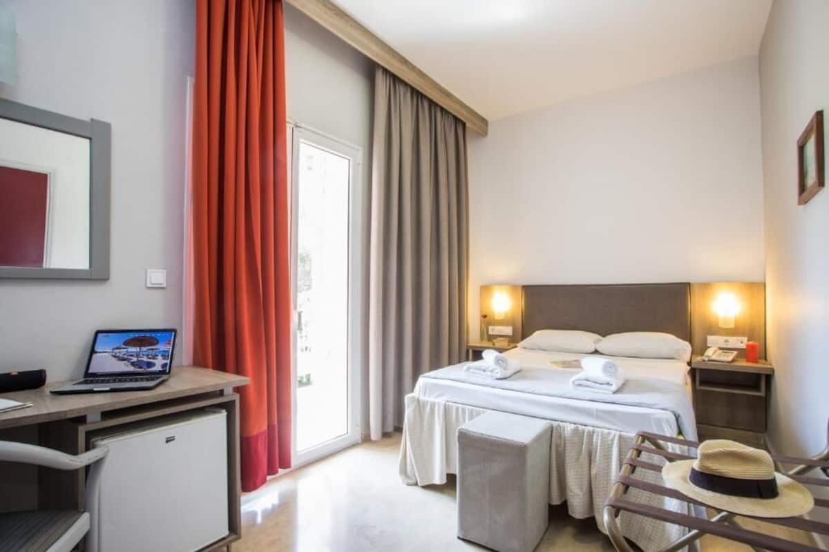 Habitación de hotel con cama, escritorio, ordenador portátil y un pequeño refrigerador.