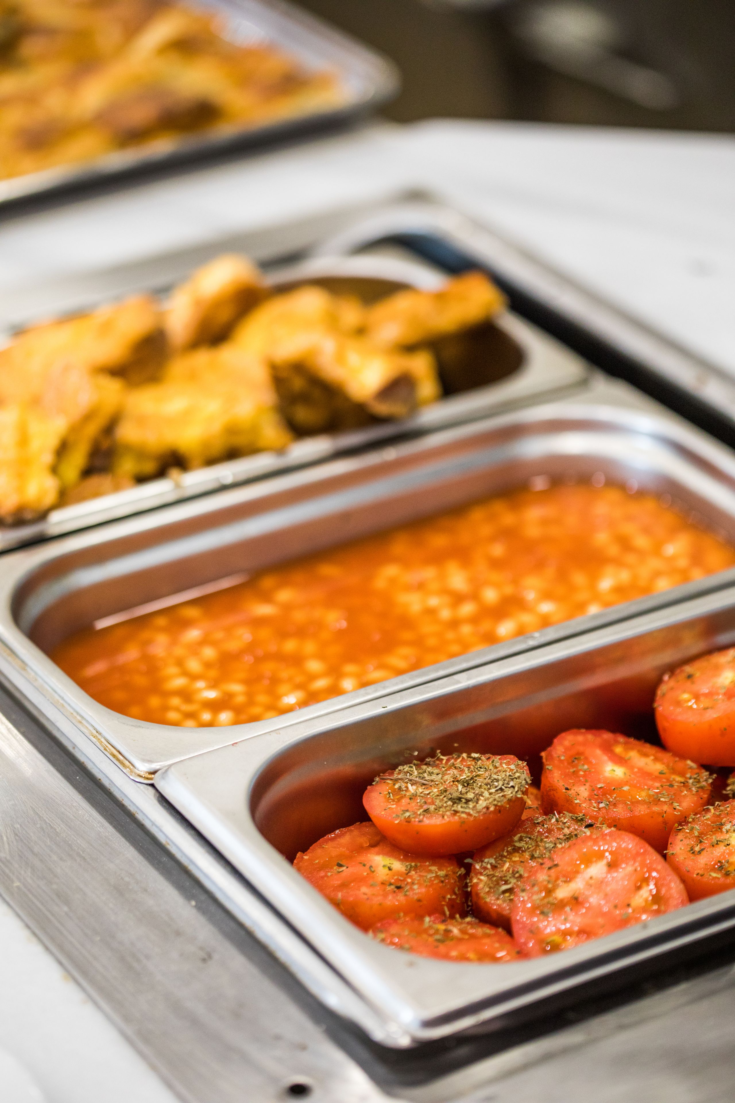 A buffet with various food options including sliced tomatoes, a red sauce, and fried items.