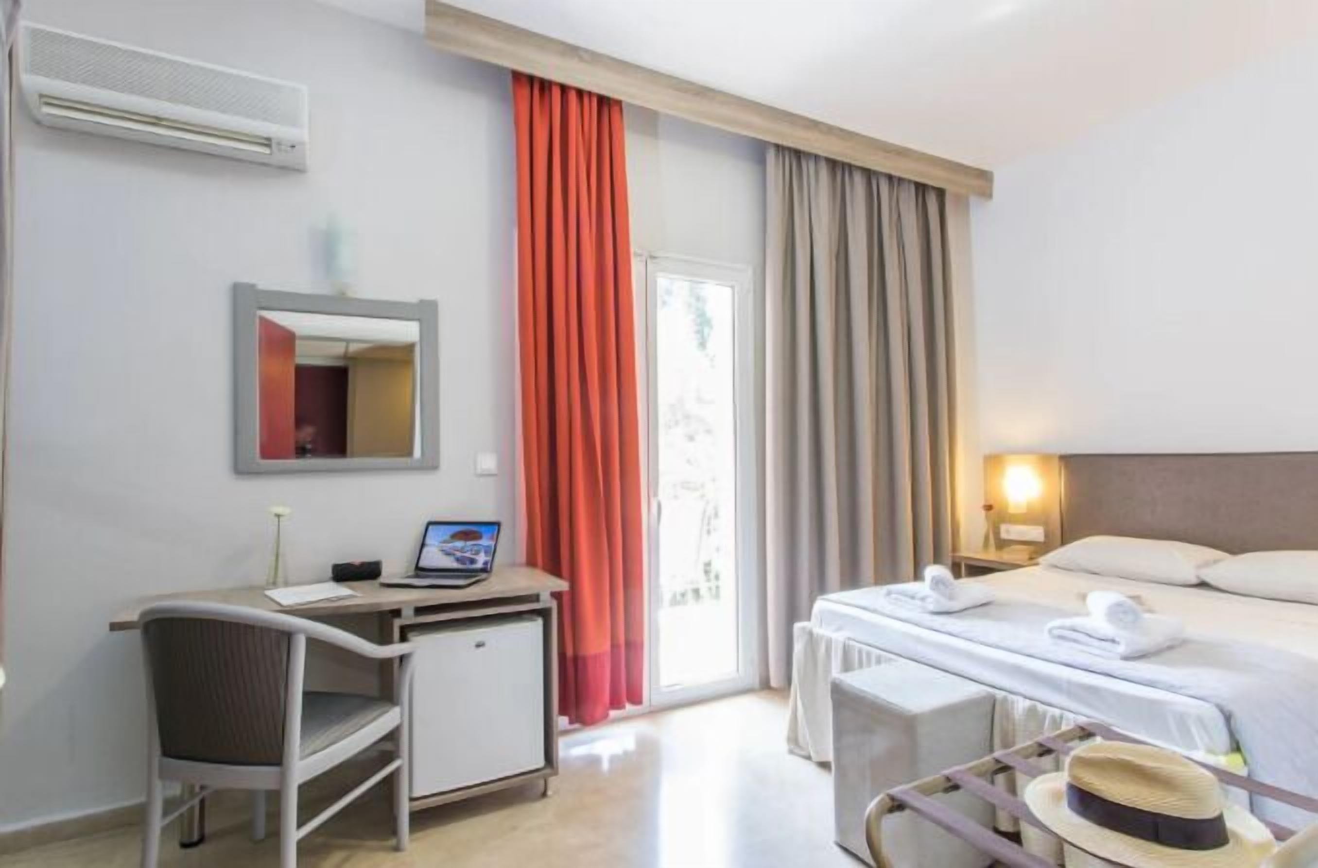 Una camera d'albergo con una scrivania, una sedia, un letto e uno specchio.