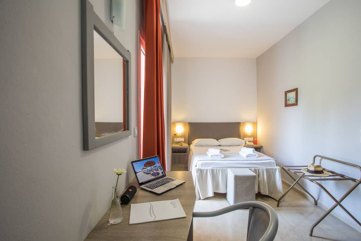 Una habitación de hotel con cama, mesita de noche, computadora portátil y escritorio con silla.