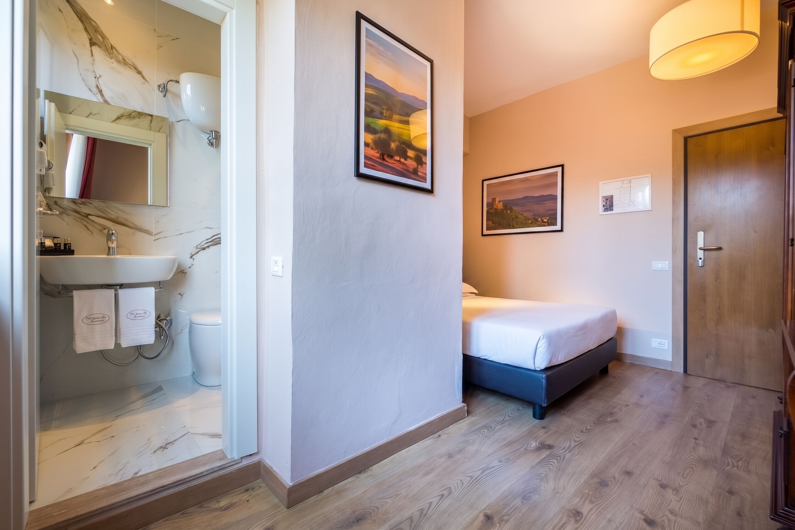 A hotel room with a bed, a bathroom with a sink and mirror, and two framed pictures on the wall.