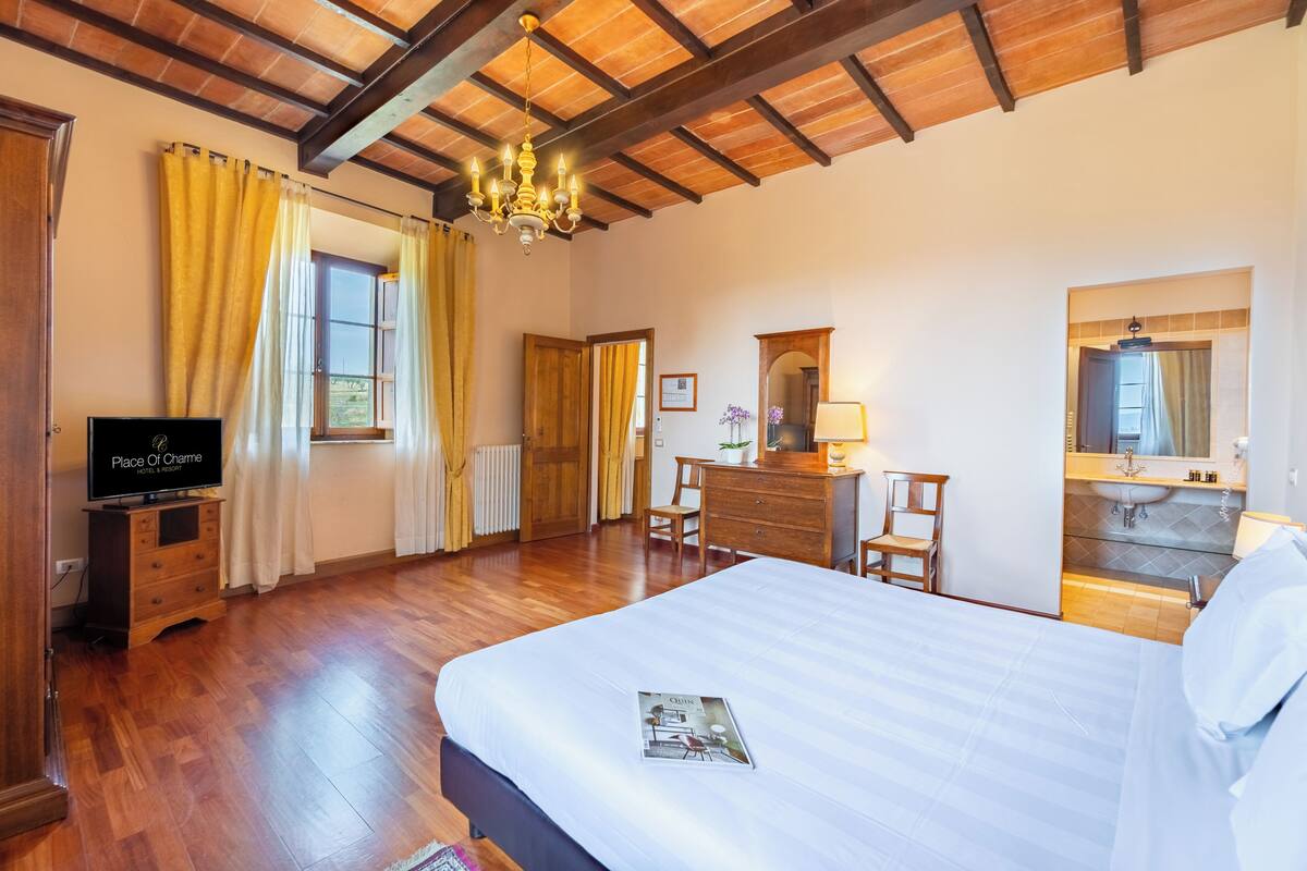 Habitación de hotel con techo de madera, cama, televisor, escritorio, silla, cómoda y baño con espejo y lavabo.