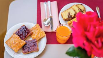 Ein Frühstückstisch mit Toast, Marmelade, einem Glas Orangensaft und einer rosa Blume.