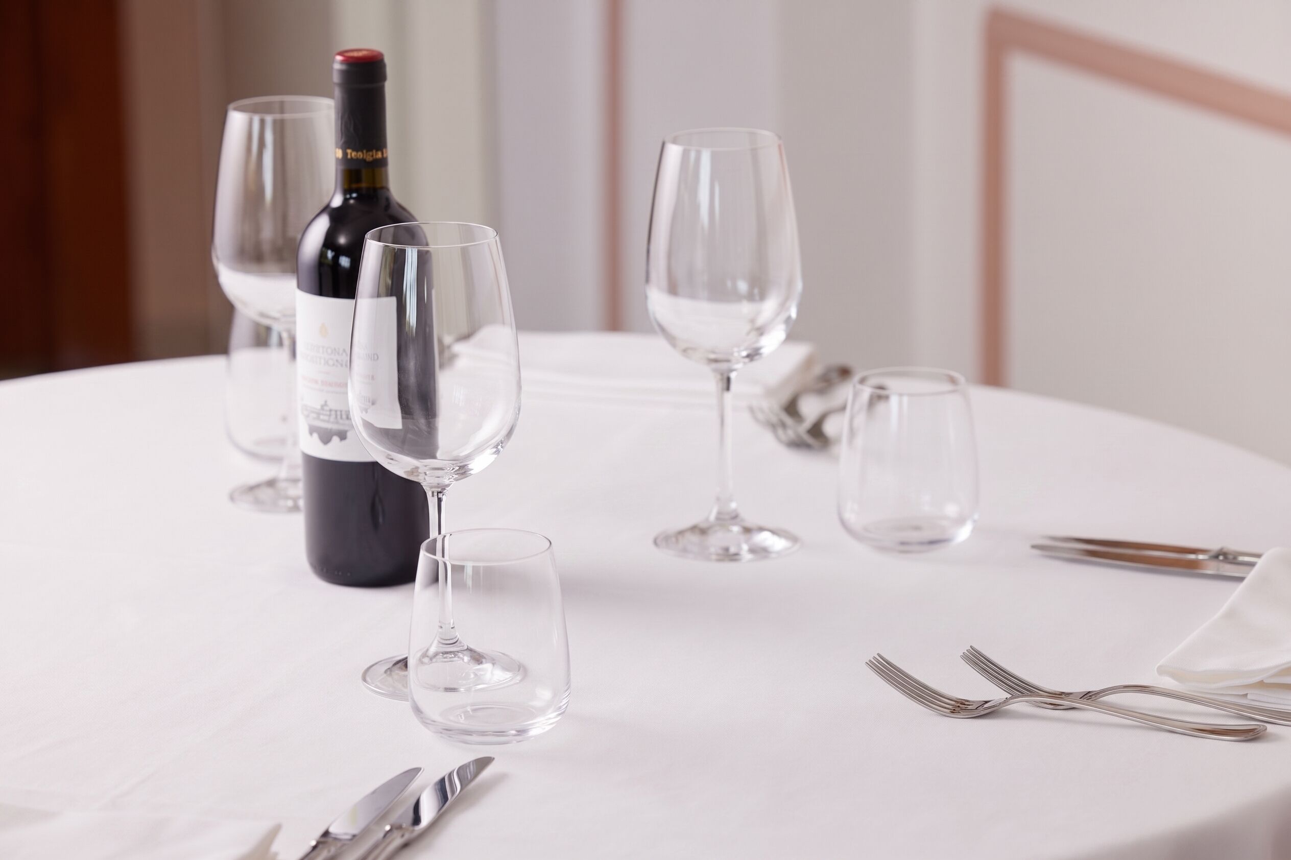A table set with wine glasses, a bottle, and cutlery.