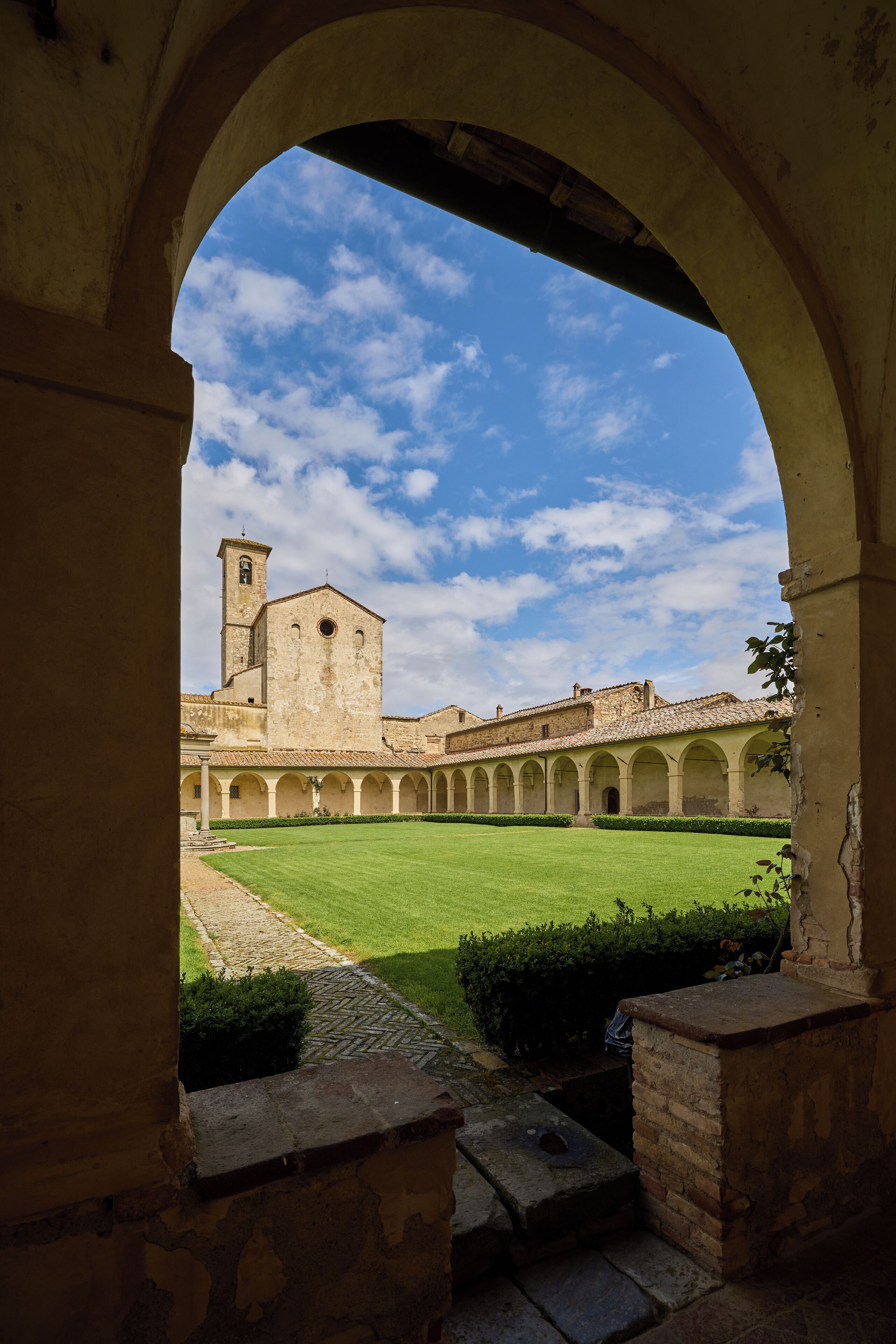 Un corredor arqueado con un patio interior y un edificio con torre al fondo.