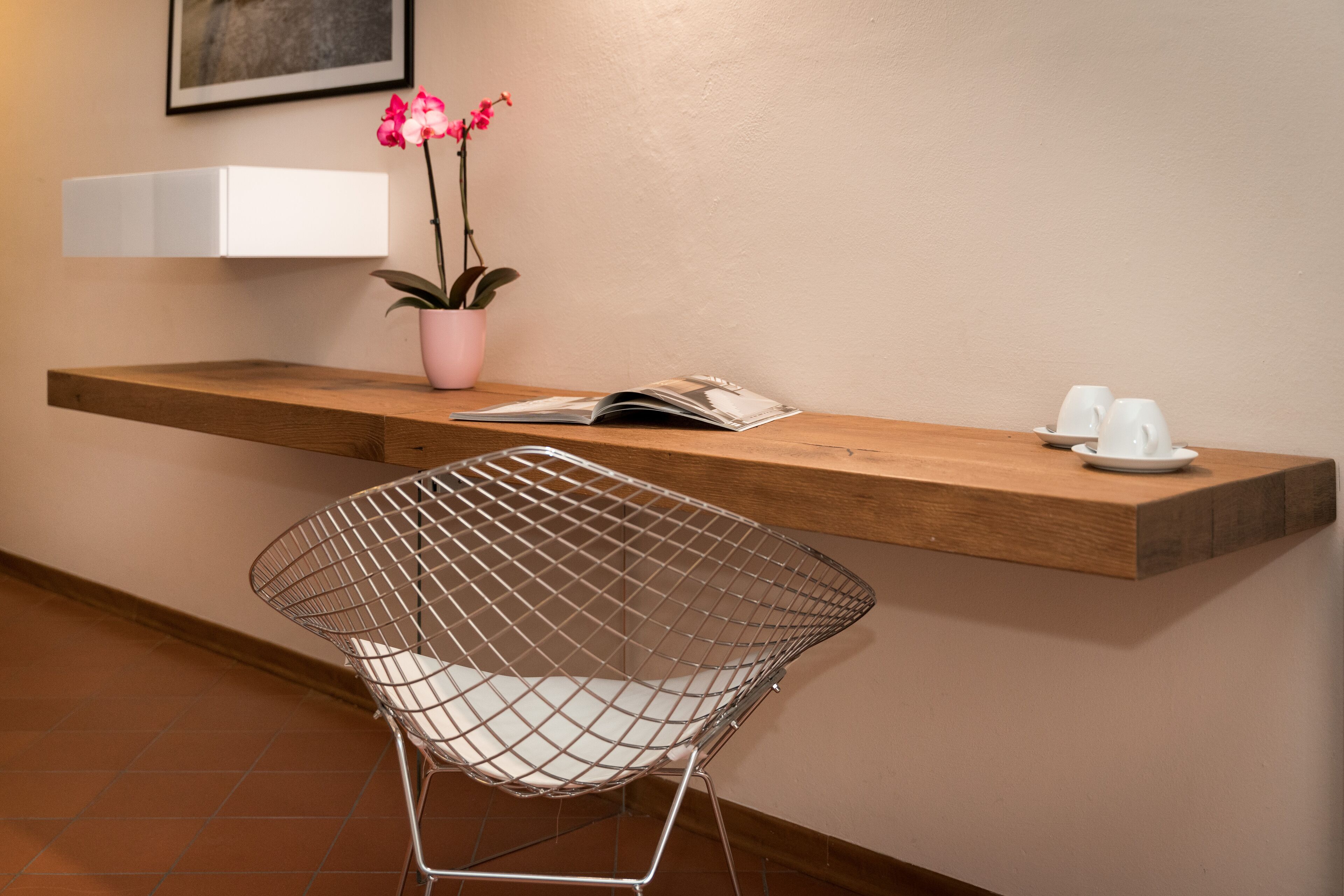 Un área de recepción moderna con un mostrador de madera, una silla de metal, una orquídea en maceta y una revista.