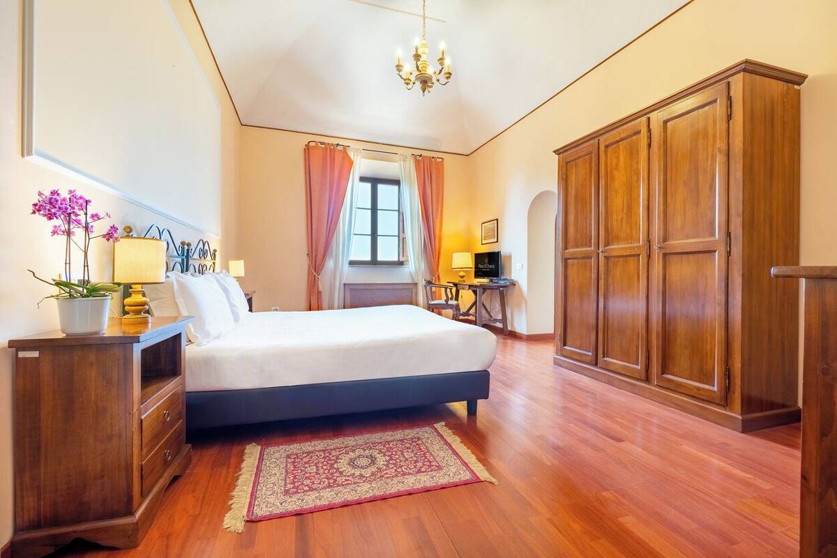 Un dormitorio con una cama, armario de madera, escritorio con lámpara y ventana con cortinas.