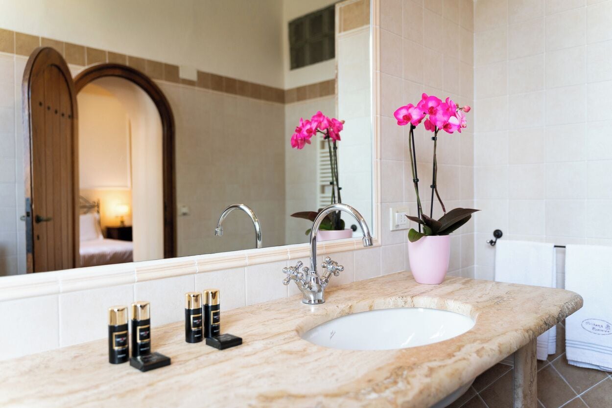 Une salle de bain avec un lavabo en marbre, un miroir, une plante orchidée rose et un porte-serviettes.
