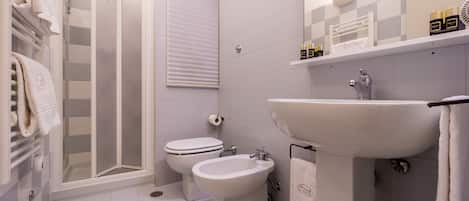 A modern bathroom with a glass shower enclosure, a toilet, a bidet, and a sink.