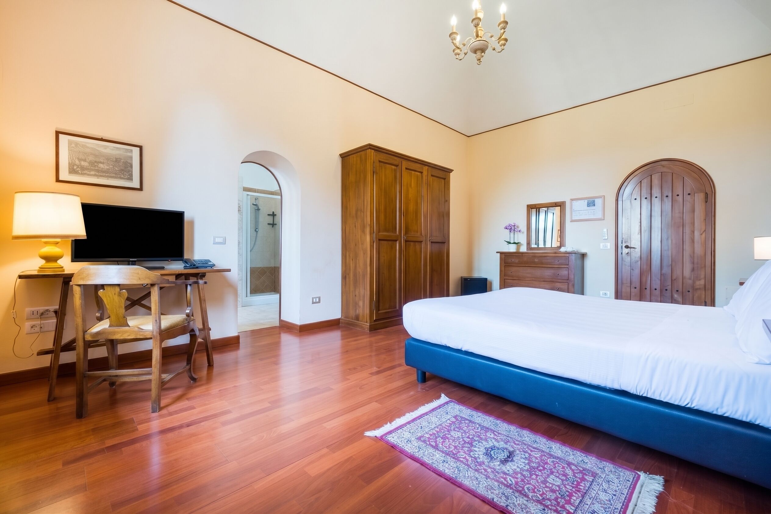 Une chambre à coucher comprenant un lit, un bureau avec un ordinateur, une chaise, une armoire et un lustre.