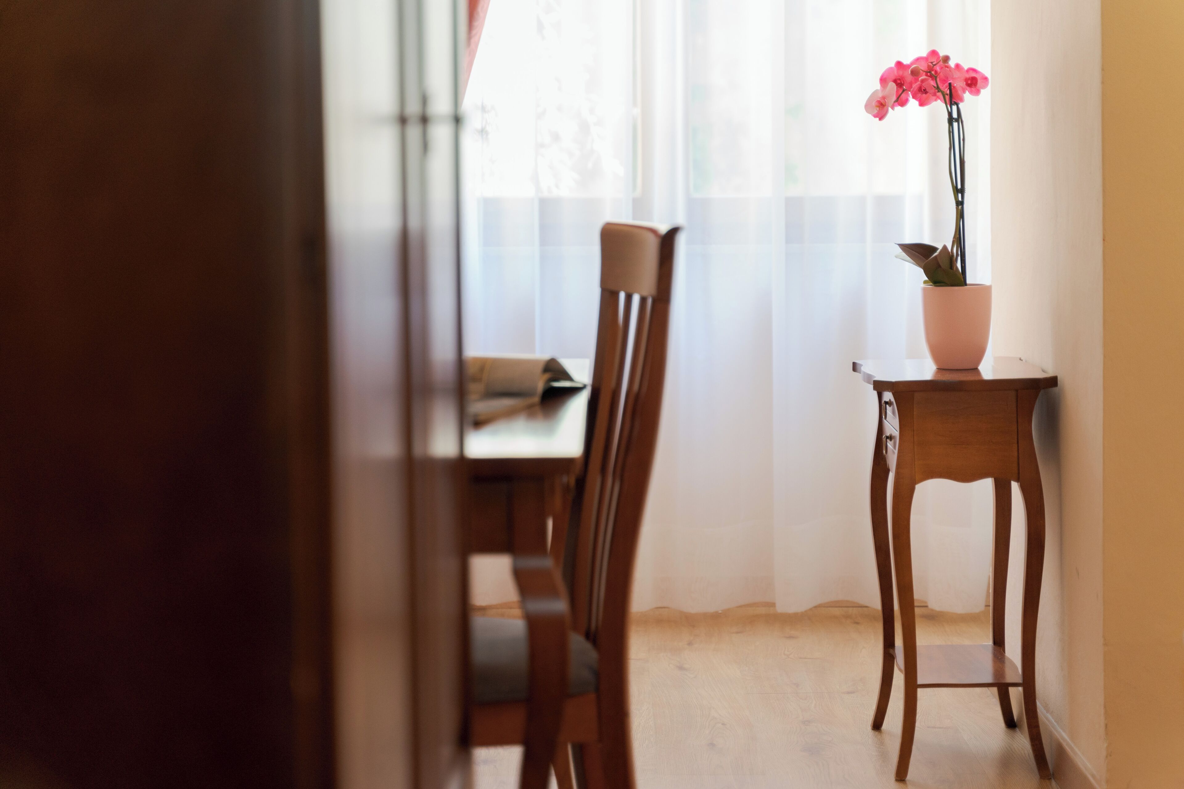Une chaise en bois et une petite table avec un pot de plante dans une pièce dotée d’une fenêtre.