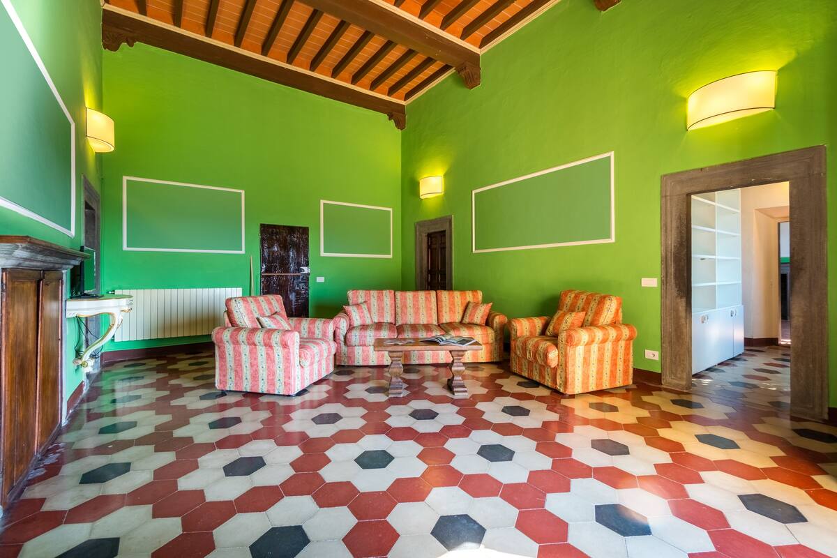 Una sala de estar con una pared verde, un piso estampado y un techo de madera.