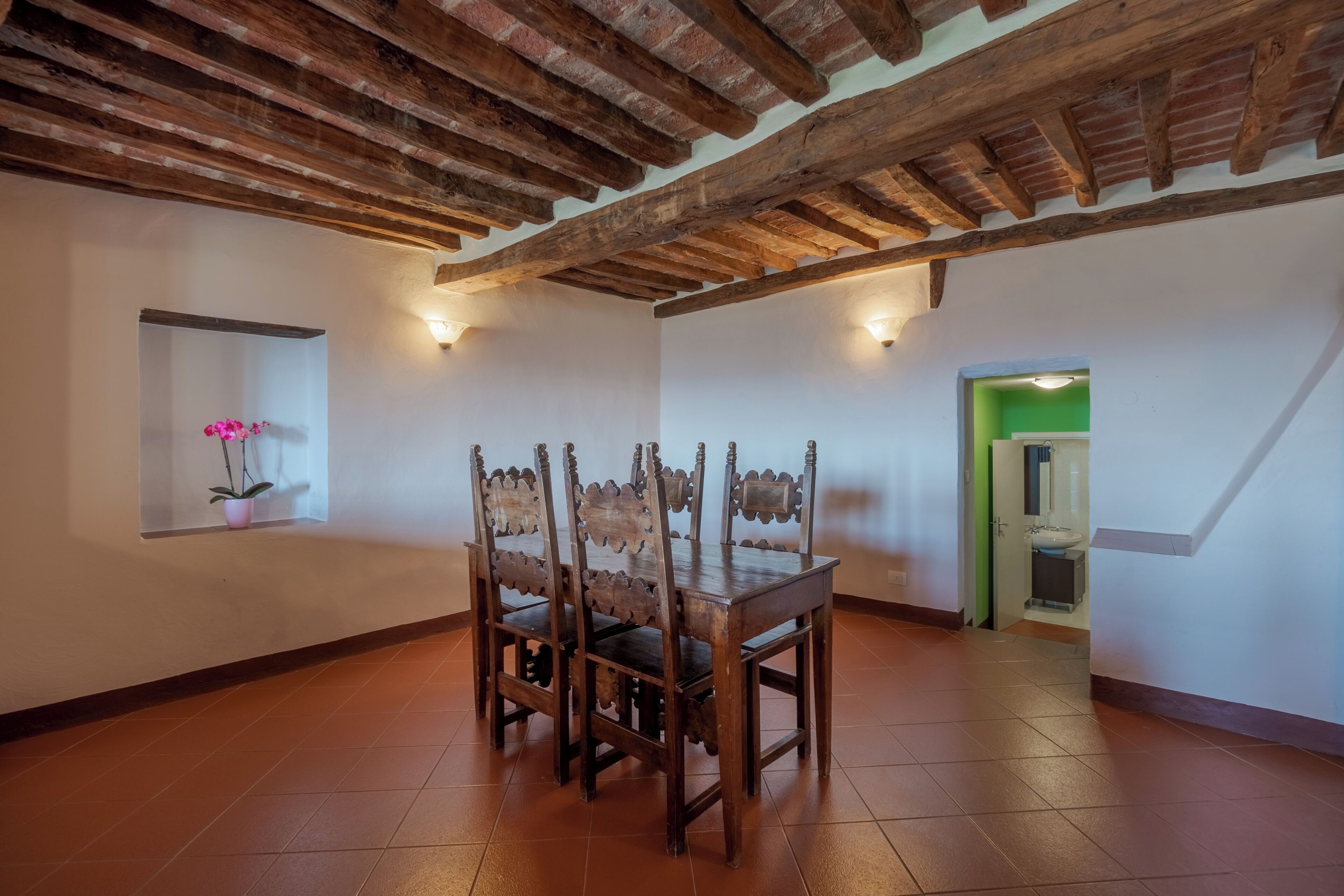 Un coin repas avec une table et des chaises en bois, une plante en pot et une porte verte donnant sur une autre pièce.