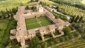 Eine Vogelperspektive zeigt einen historischen Gebäudekomplex mit einem zentralen Innenhof, umgeben von Weinbergen und Grünflächen.