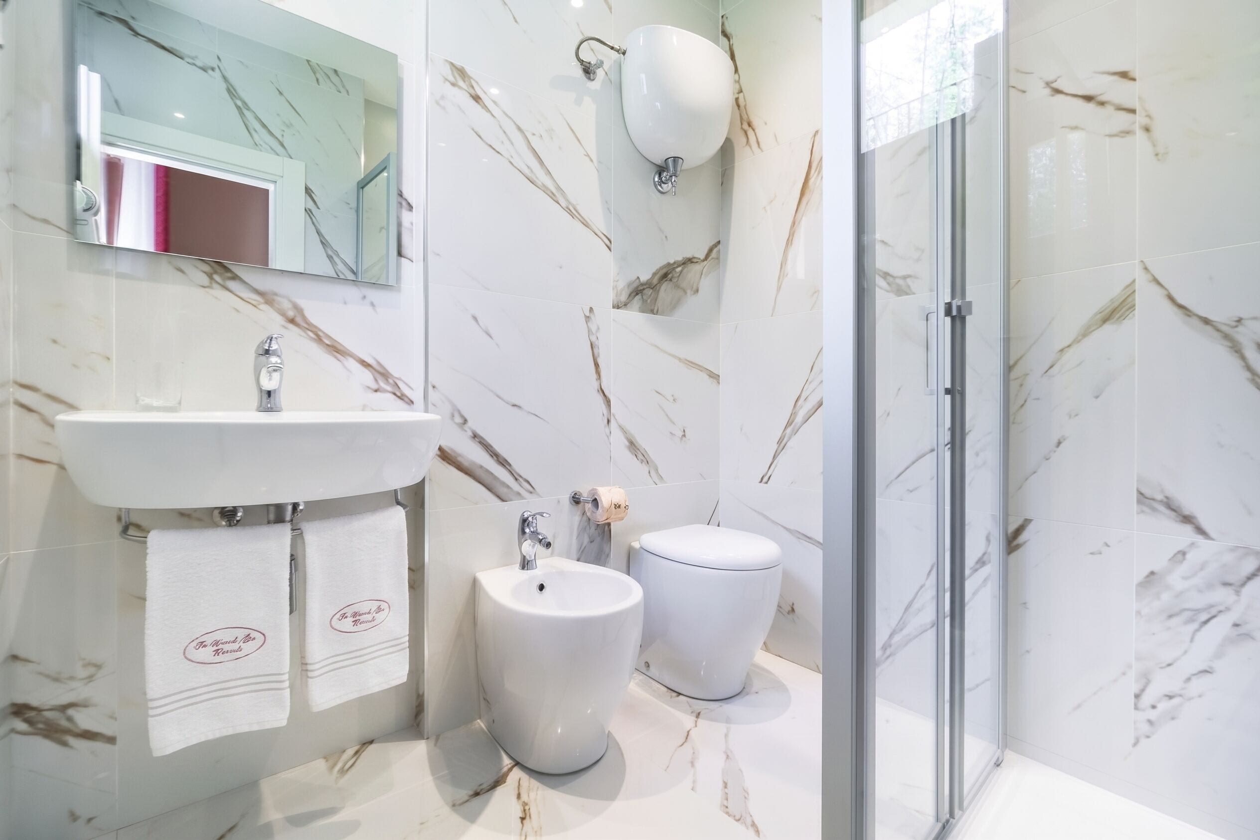 Un bagno moderno con zoccolo in marmo, lavabo, bidet e cabina doccia in vetro.