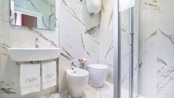 Un bagno moderno con zoccolo in marmo, lavabo, bidet e cabina doccia in vetro.