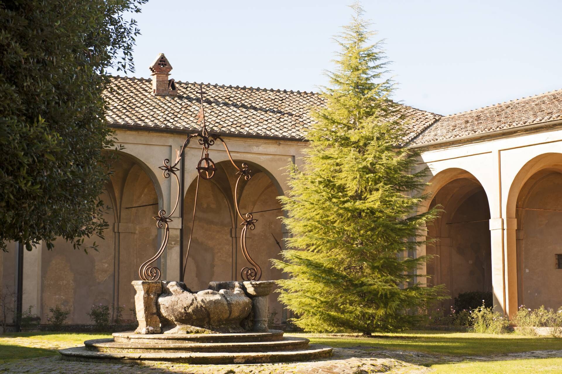 A courtyard with a stone fountain, arched walkways, and a tall evergreen tree.