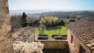 Ein Innenhof mit Blick auf ein grünes Feld und ferne Hügel, umgeben von Steingebäuden mit Terrakotta-Dächern.