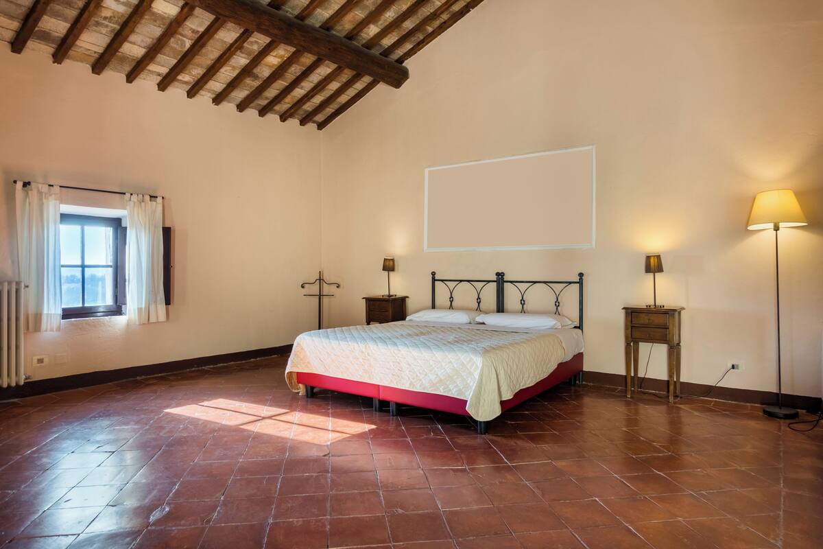Un dormitorio con una cama, una ventana con cortinas, un radiador y un techo de madera.