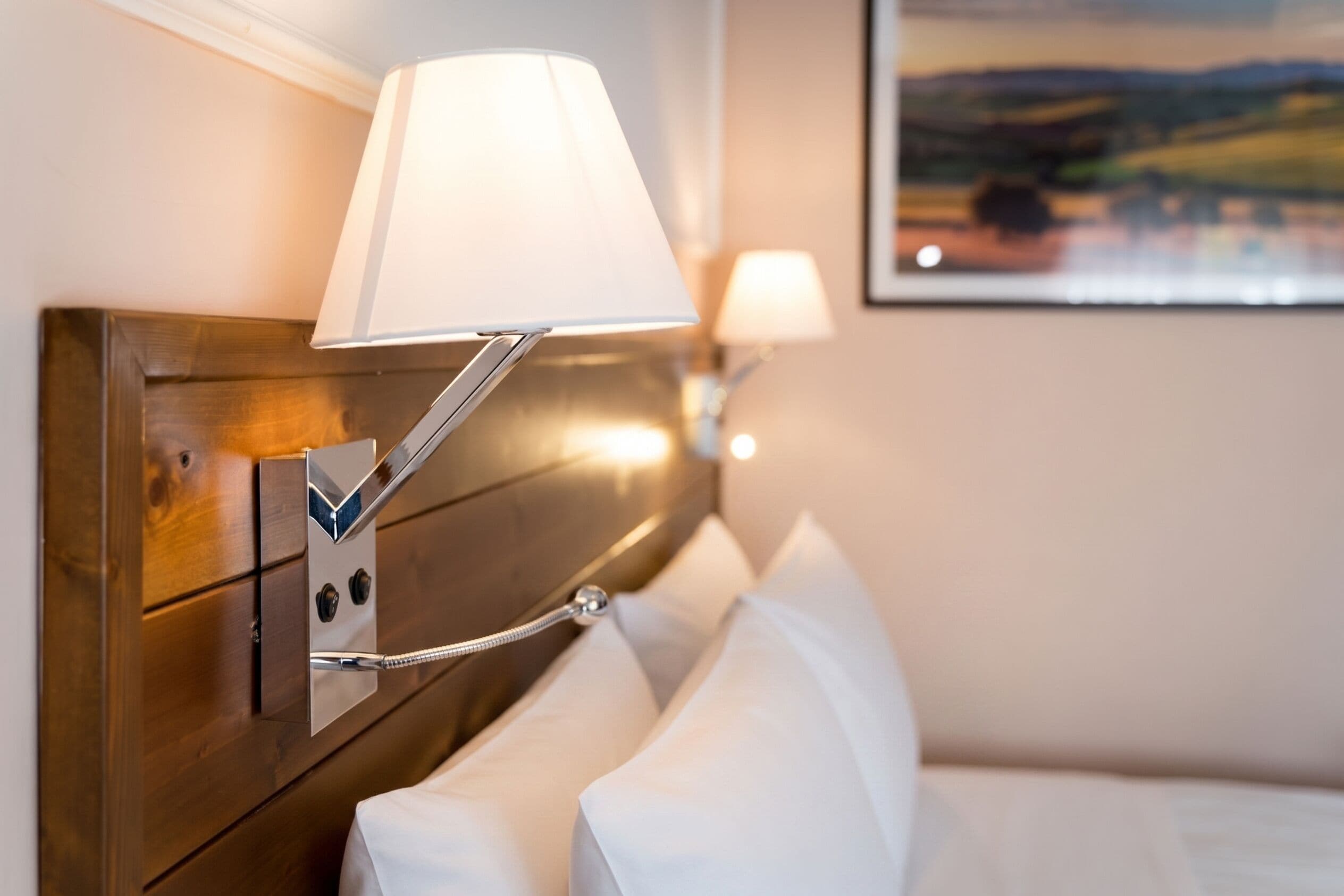 Una habitación de hotel con cabecera de madera, una lámpara de pared y un cuadro de un paisaje.
