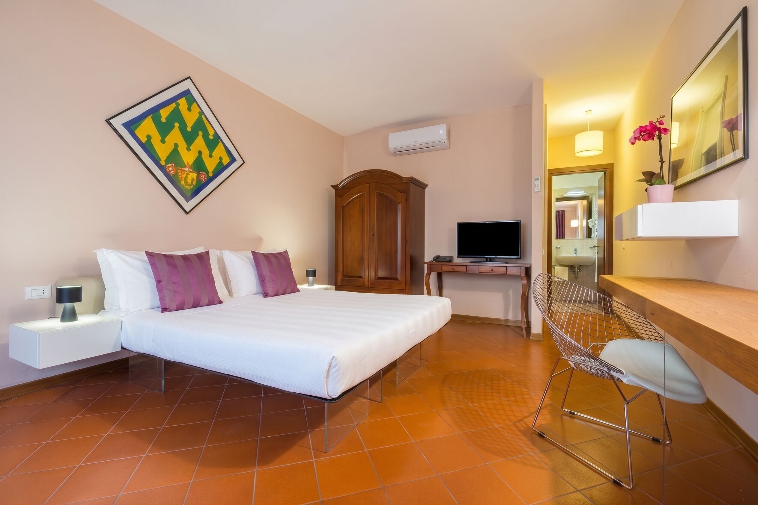 Ein Hotelzimmer mit Bett, Schreibtisch, Stuhl, Fernseher, Kleiderschrank und Spiegel.