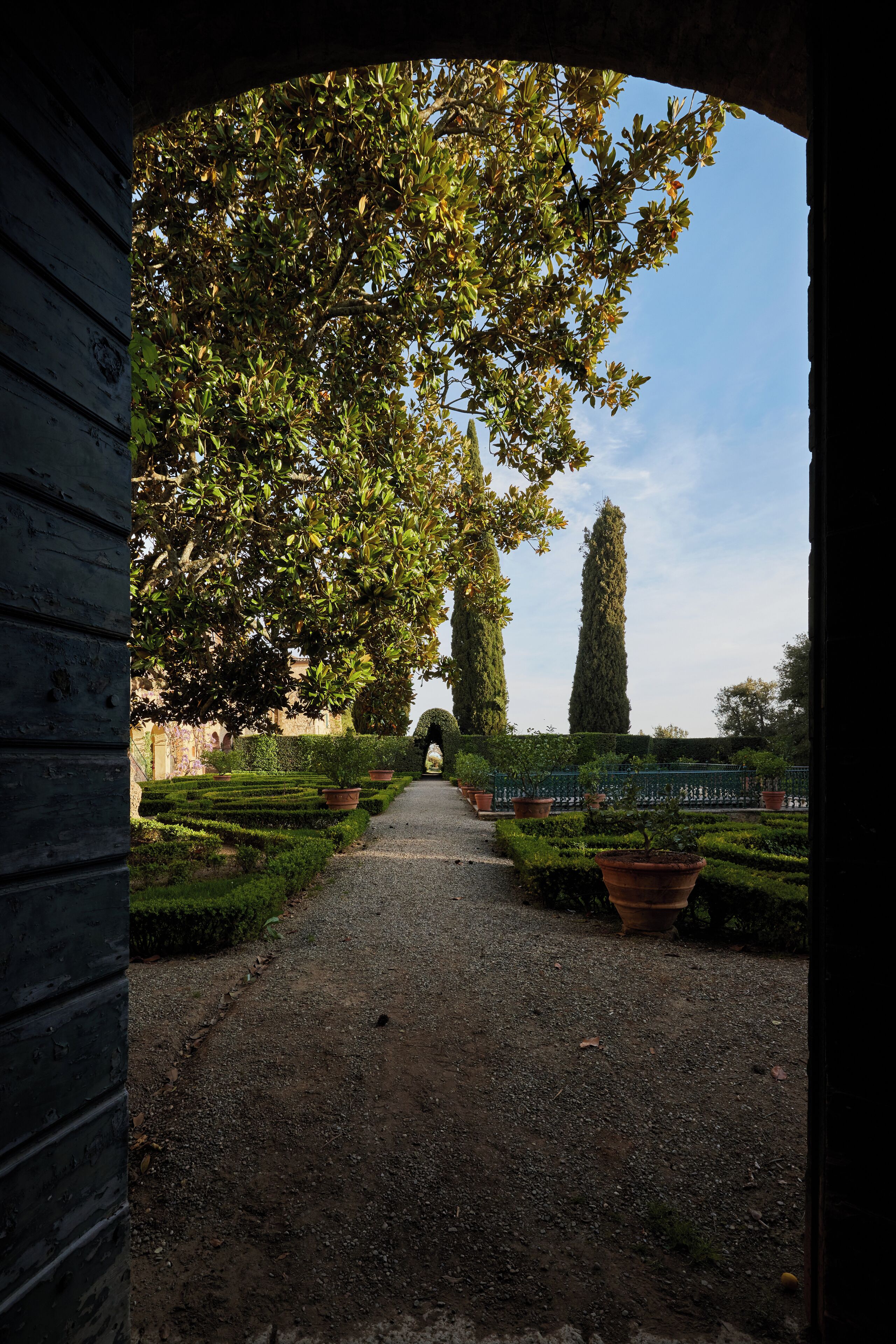 A pathway leading through a garden with neatly trimmed hedges and tall trees.