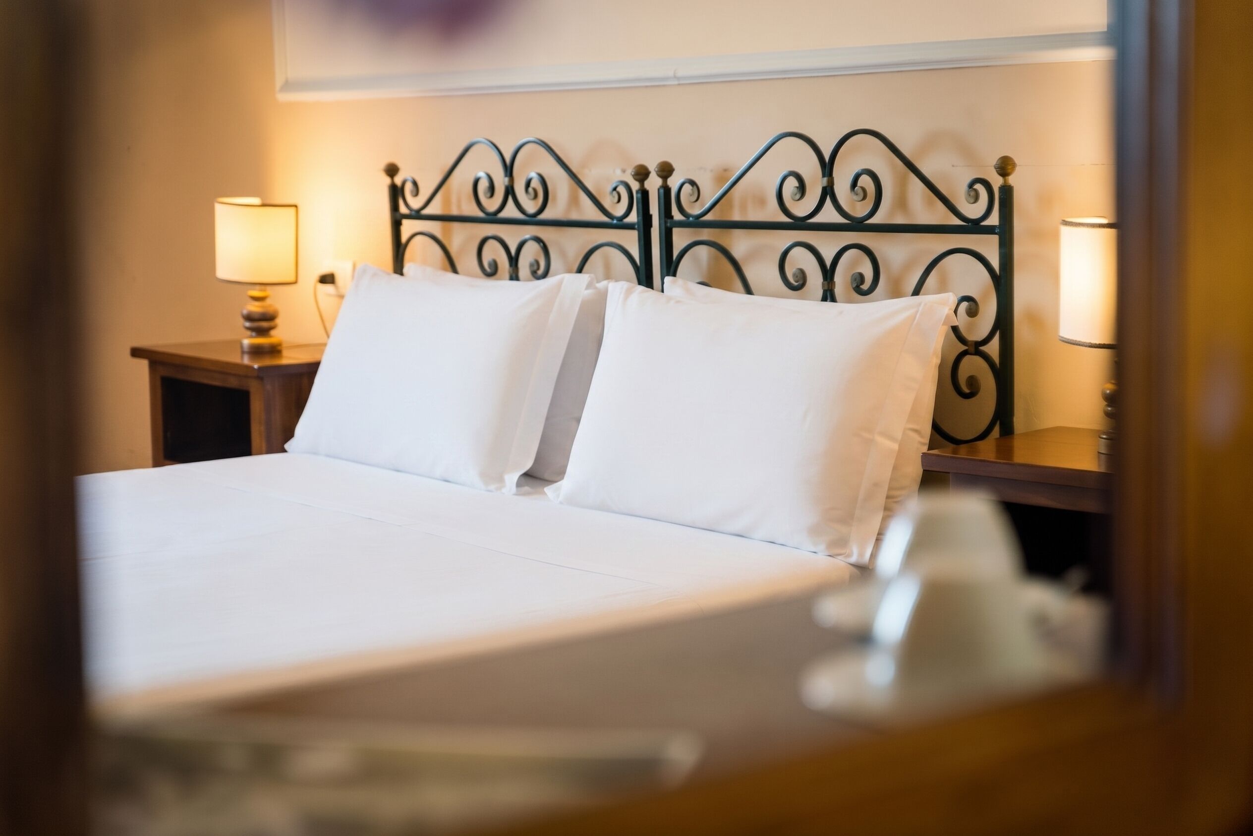 Una cama bien hecha con sábanas blancas, dos lámparas de noche y un cabecero decorativo de metal.