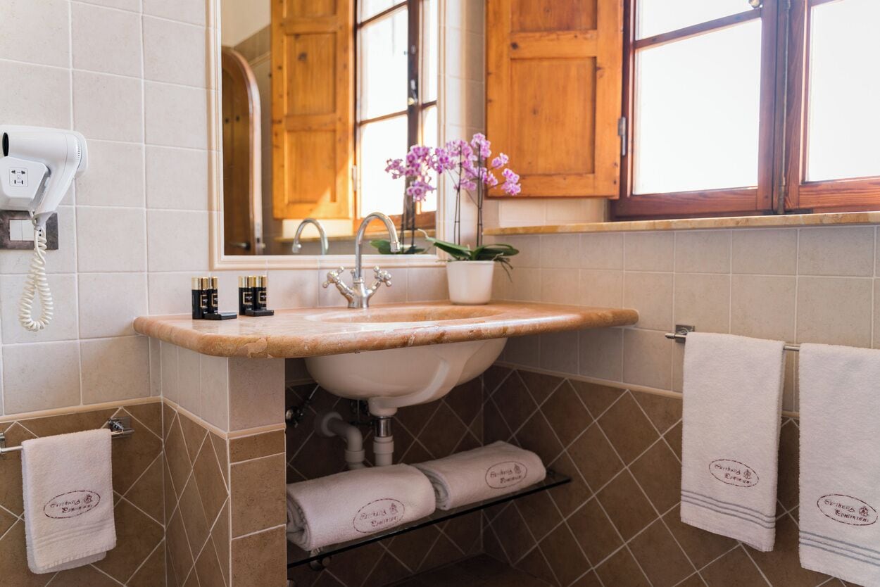 A bathroom with a sink, mirror, and a telephone. There are towels and a potted orchid.