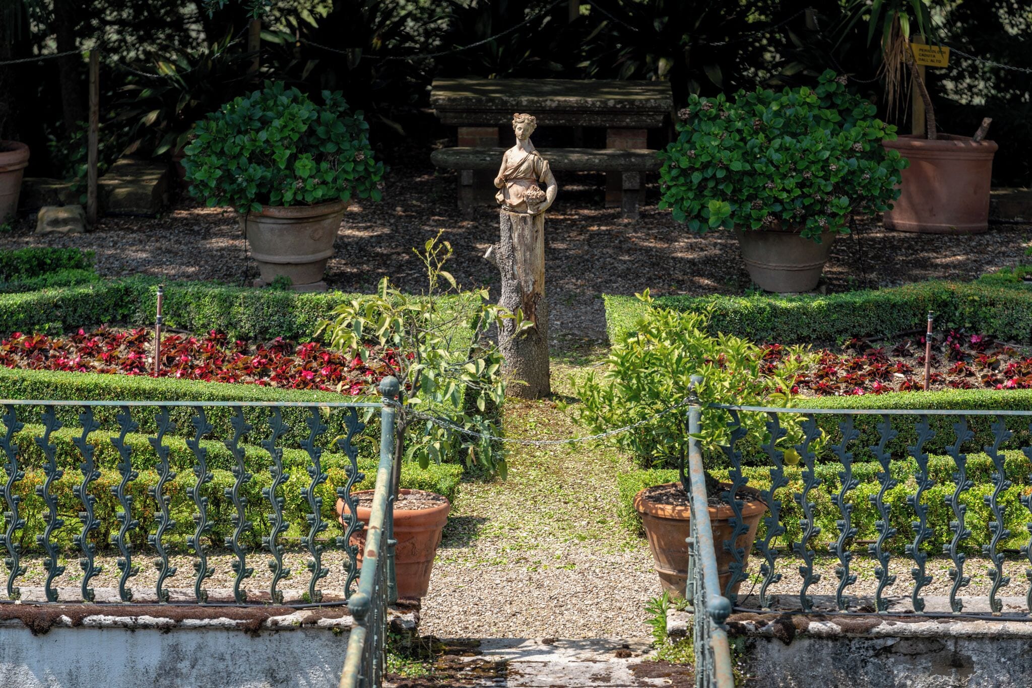 A garden with a statue, potted plants, and a gravel path.