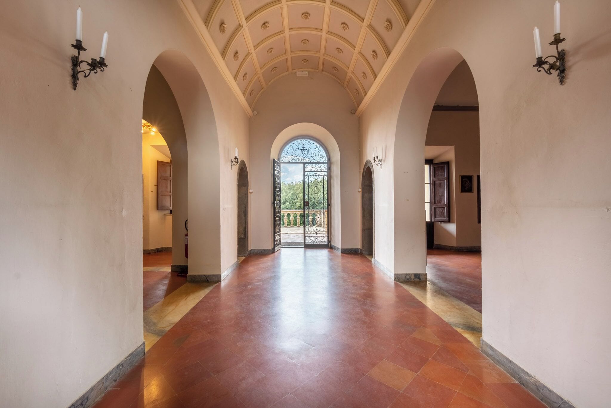 Ein Korridor mit Fliesenboden, gewölbter Decke und Wandleuchtern.