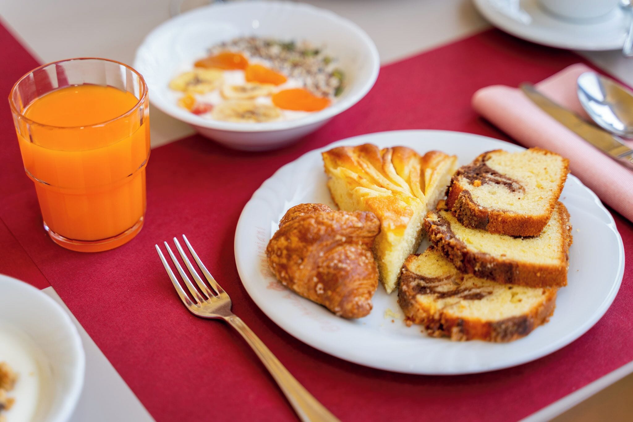 Un desayuno con una fuente de pan, un croissant y un vaso de jugo de naranja.