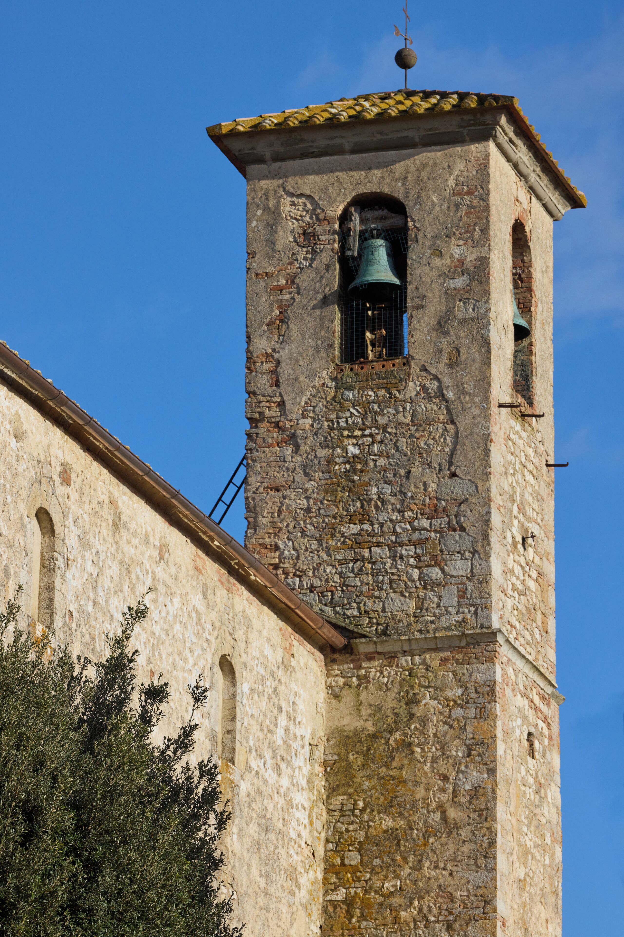 Una histórica torre de campana de piedra, con veleta, campana y una pequeña ventana.