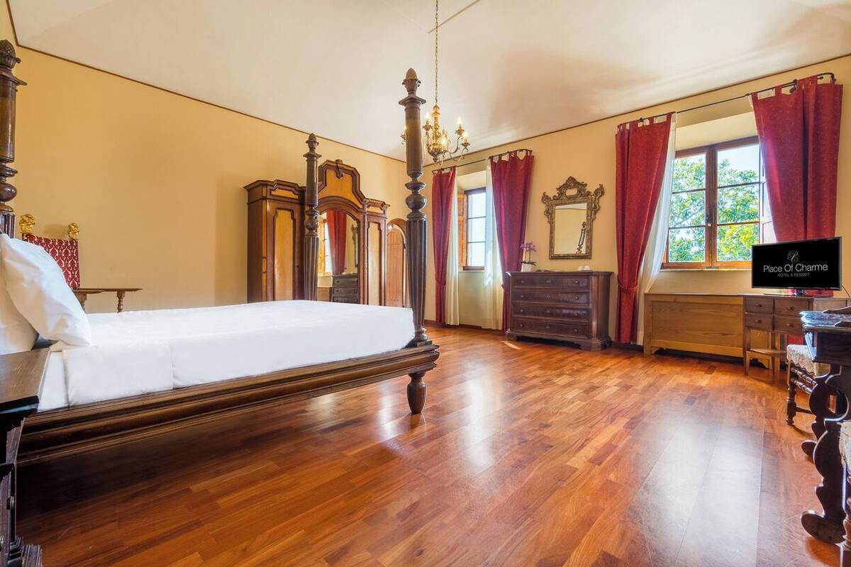 Un dormitorio con una cama grande, muebles de madera, un candelabro y una ventana con cortinas.